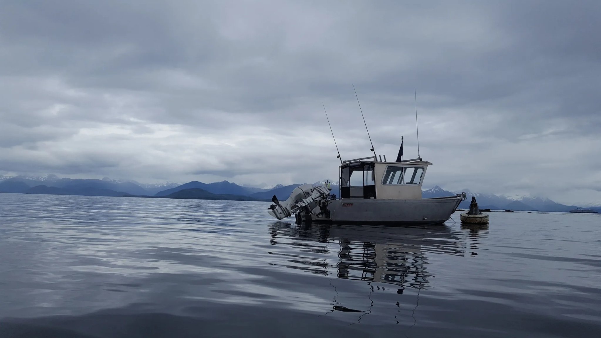Tongass Troll anchored on glassy water with snow-capped mountains reflected below
