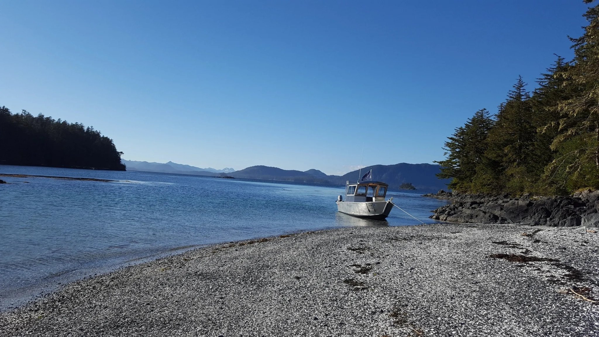 Tongass Troll anchored on a pristine Alaskan beach with mountains in the distance
