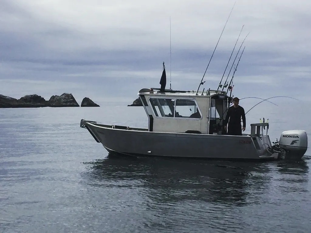 Capt. Xander standing at the stern with fishing rods bent, rocky islands in the background