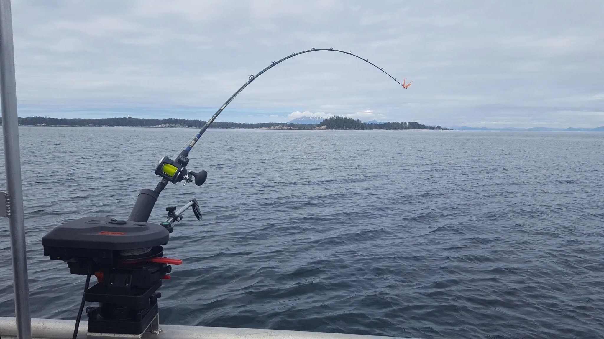 Fishing rod bent hard with a fish on, Sitka Sound islands in the background